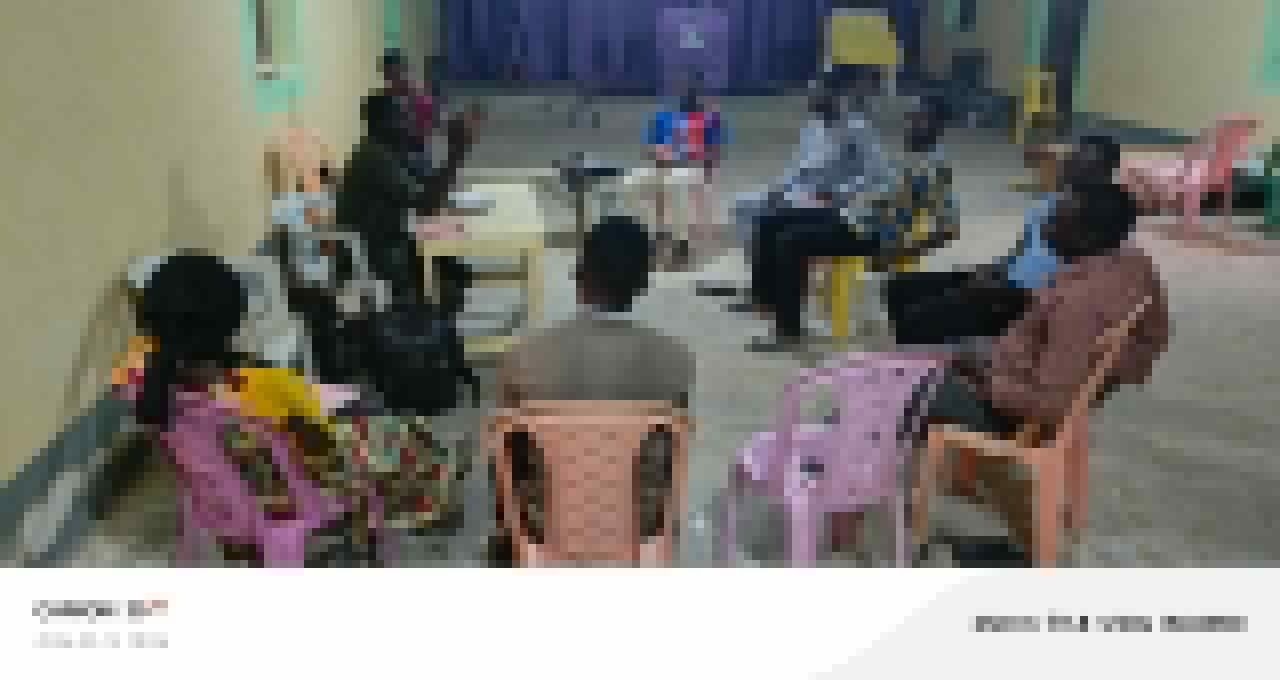 The Abeche Center indoors. People seated in plastic chairs in a long meeting hall, a small group of women in patterned dresses in the foreground, more attendees deeper into the room.