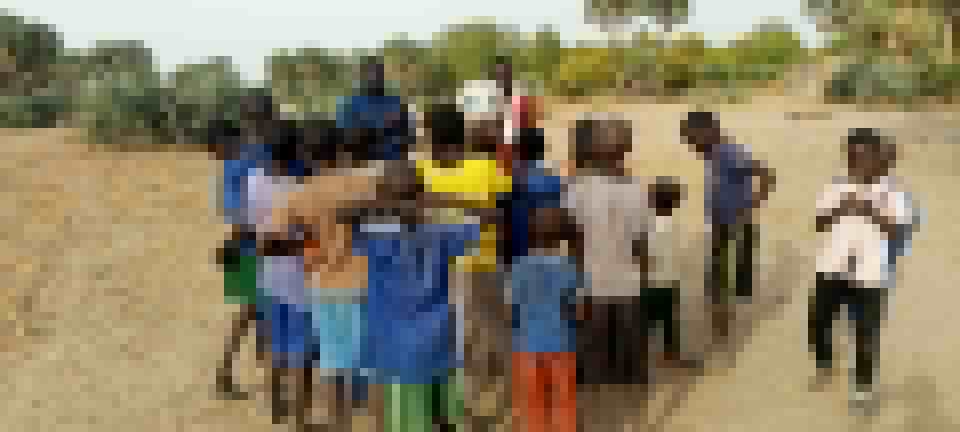 Children gathered together outdoors at the Nord Ou'est location, leaning into the camera on sandy ground.